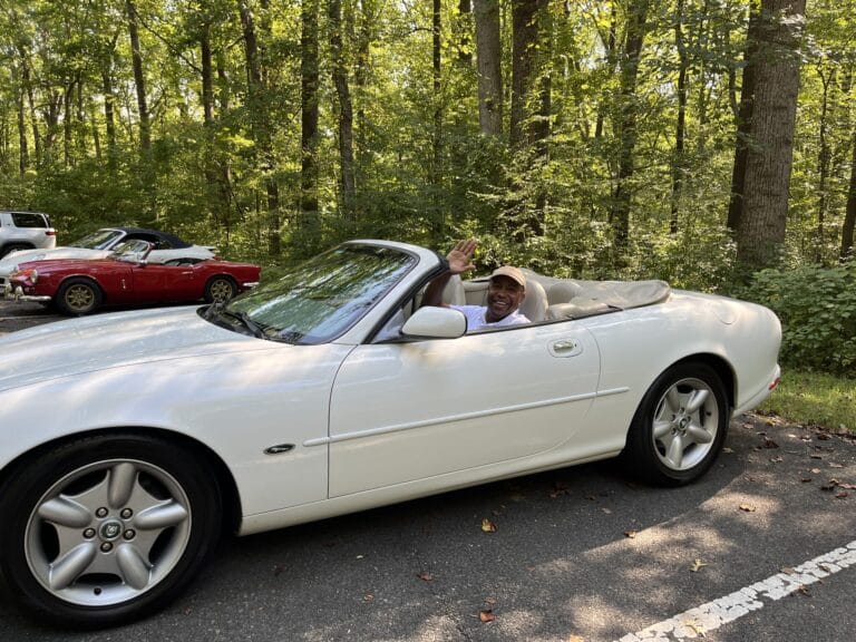 A club member waving from behind the wheel of a white Jaguar convertible at the 2026 Test Drive